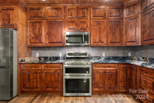 kitchen featuring dark stone countertops, light hardwood / wood-style flooring, stainless steel appliances, and backsplash