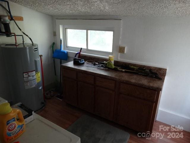 kitchen with dark hardwood / wood-style floors, dark brown cabinets, electric water heater, and a textured ceiling