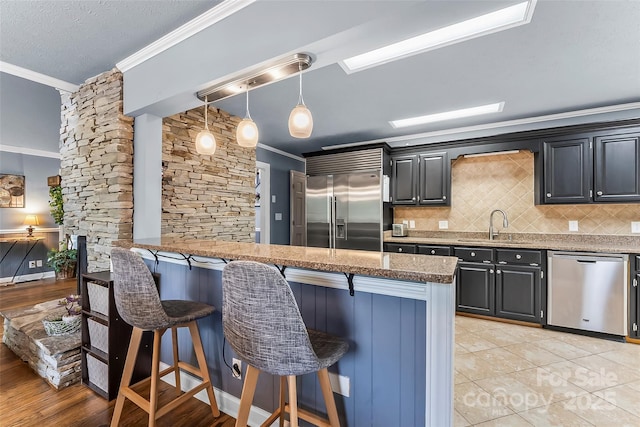 kitchen with decorative light fixtures, a breakfast bar, sink, appliances with stainless steel finishes, and ornamental molding