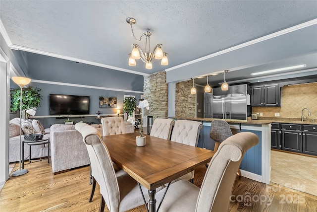 dining area with a notable chandelier, a textured ceiling, ornamental molding, light hardwood / wood-style flooring, and sink