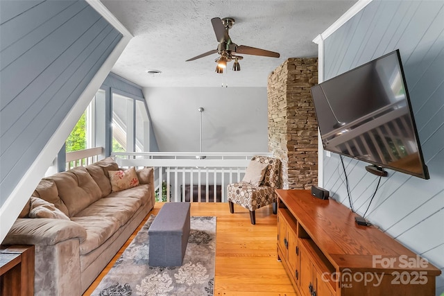 living room featuring ceiling fan, a textured ceiling, light hardwood / wood-style flooring, and wood walls