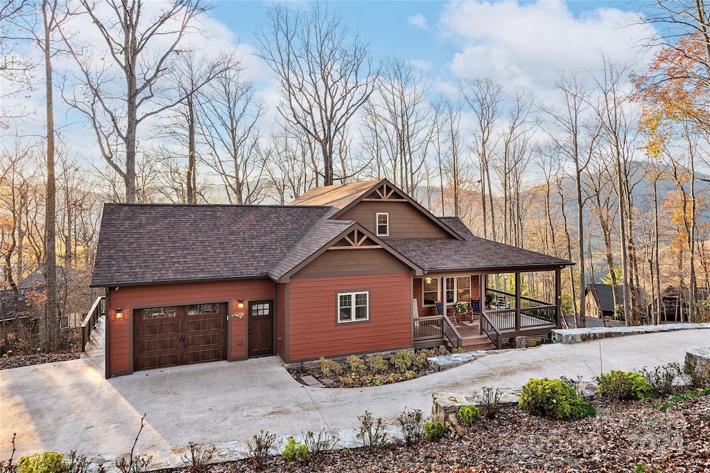 rustic home featuring a porch, driveway, a shingled roof, and a garage