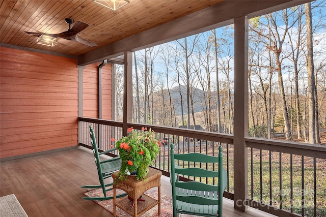 unfurnished sunroom featuring plenty of natural light, ceiling fan, a mountain view, and wood ceiling