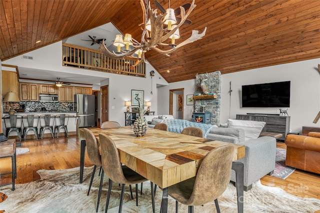 dining area featuring a fireplace, light wood-type flooring, wood ceiling, ceiling fan with notable chandelier, and a towering ceiling