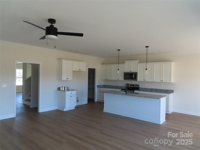 kitchen with appliances with stainless steel finishes, white cabinetry, sink, dark stone countertops, and a kitchen island with sink