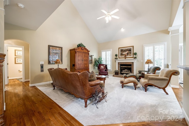 living room with wood-type flooring, ceiling fan, high vaulted ceiling, and a fireplace