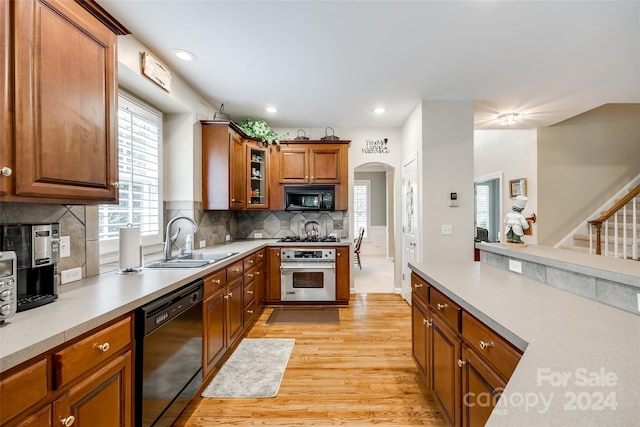 kitchen featuring light wood-type flooring, black appliances, backsplash, and sink