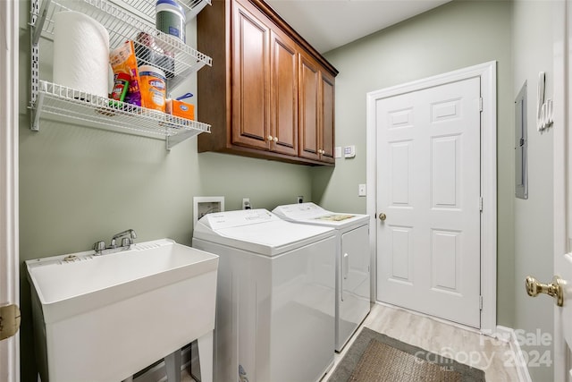 clothes washing area with cabinets, sink, electric panel, washing machine and dryer, and light wood-type flooring