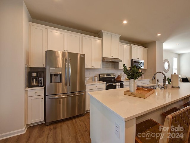 kitchen with appliances with stainless steel finishes, wood-type flooring, tasteful backsplash, white cabinets, and sink