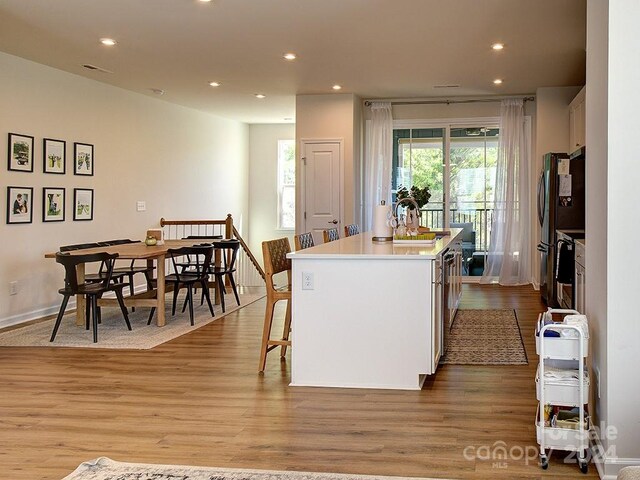 kitchen with stainless steel refrigerator, a kitchen breakfast bar, light hardwood / wood-style floors, and a kitchen island with sink