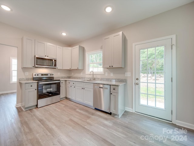 kitchen with light stone counters, sink, white cabinetry, light hardwood / wood-style flooring, and stainless steel appliances