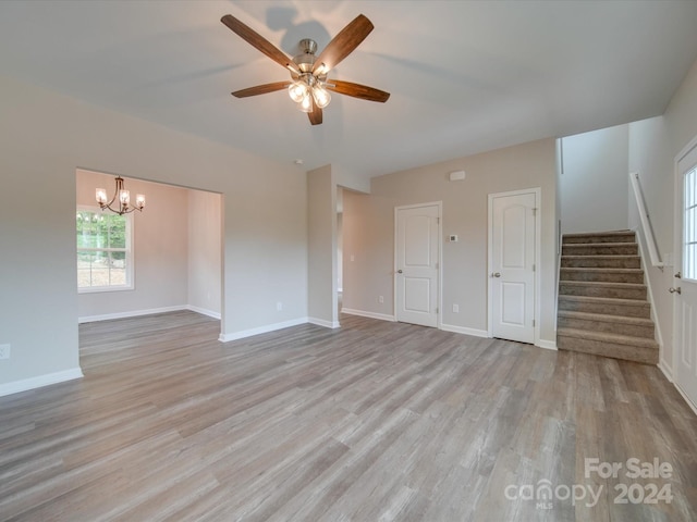 unfurnished living room featuring ceiling fan with notable chandelier and light hardwood / wood-style floors