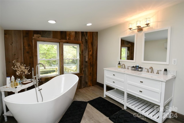 bathroom featuring oversized vanity, double sink, hardwood / wood-style floors, wooden walls, and a bathtub