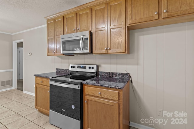 kitchen featuring stainless steel appliances, dark stone countertops, a textured ceiling, light tile floors, and ornamental molding