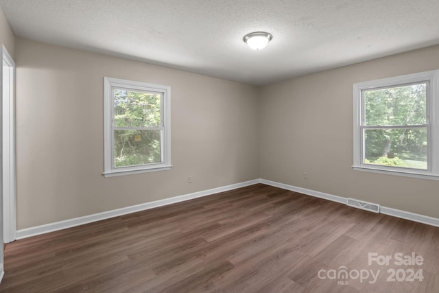 empty room with dark hardwood / wood-style floors and a textured ceiling