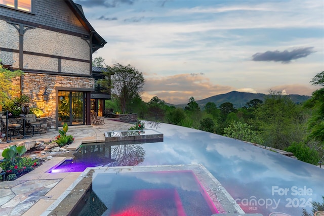 pool at dusk with a patio, an in ground hot tub, and a mountain view