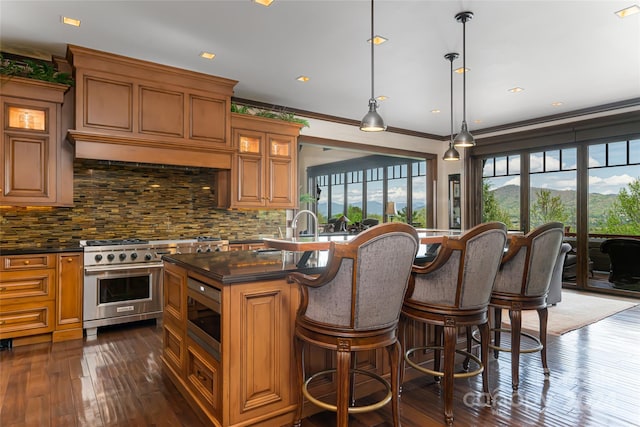 kitchen with dark hardwood / wood-style flooring, stainless steel appliances, hanging light fixtures, tasteful backsplash, and an island with sink