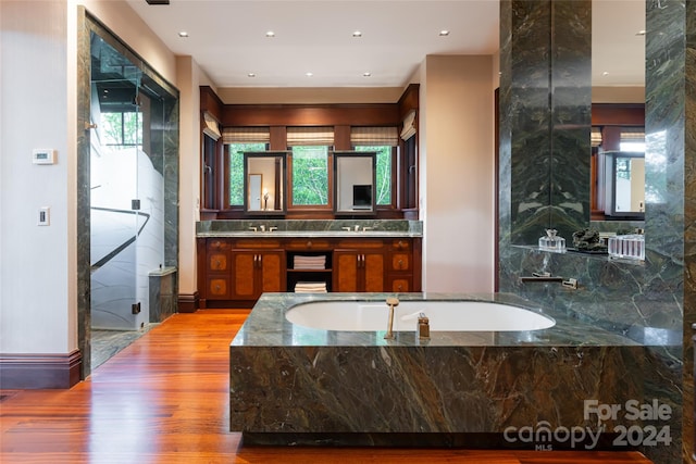 bathroom featuring plenty of natural light, hardwood / wood-style floors, tiled tub, and vanity