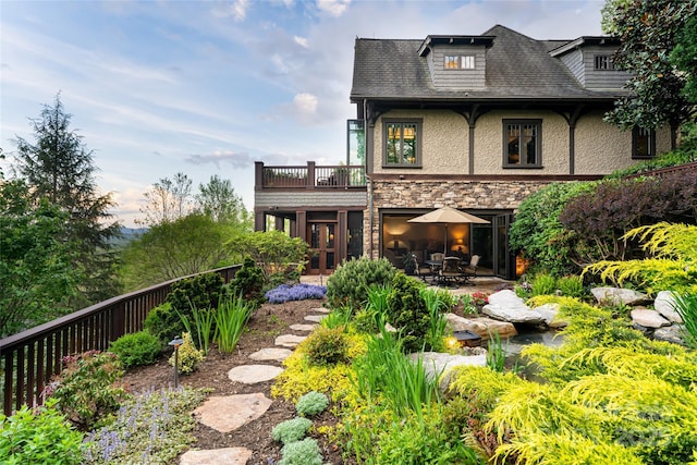 rear view of house featuring a balcony, stone siding, a patio area, and stucco siding