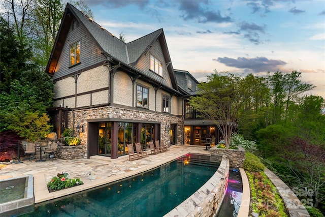 back of property at dusk with a patio, stone siding, and an outdoor pool