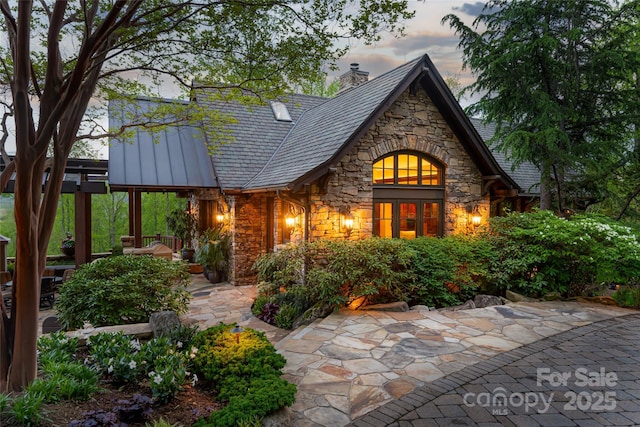 back of property with stone siding and a chimney