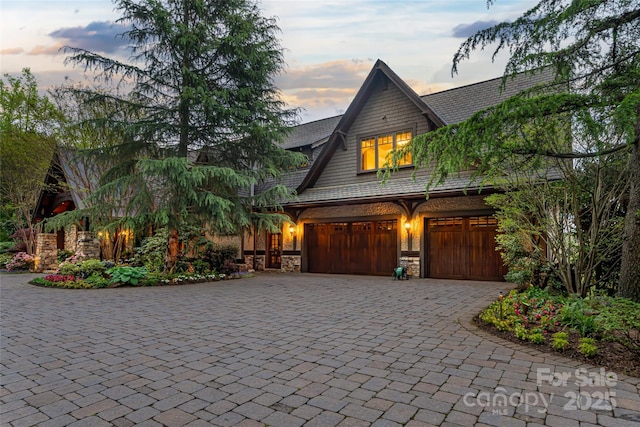 view of front facade featuring decorative driveway, stone siding, and a garage