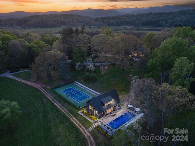 aerial view at dusk featuring a mountain view and a wooded view