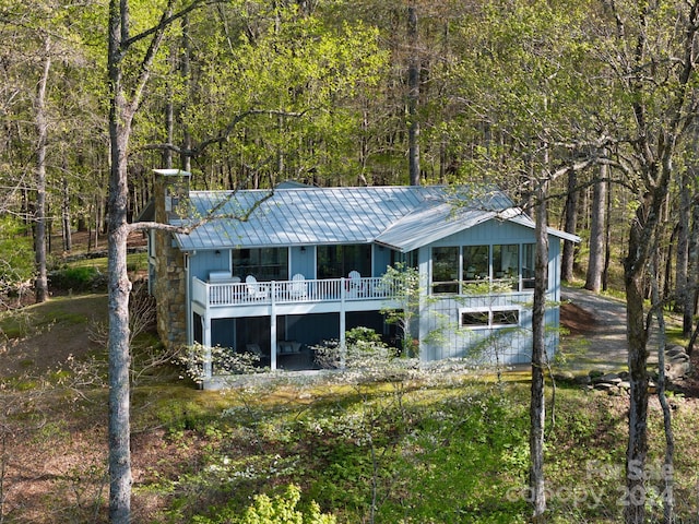 rear view of house featuring a chimney, a forest view, and metal roof