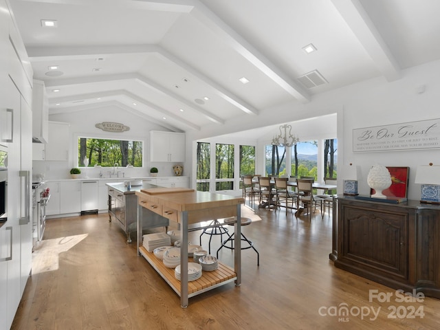 kitchen featuring beamed ceiling, high end stove, white cabinets, and light wood finished floors