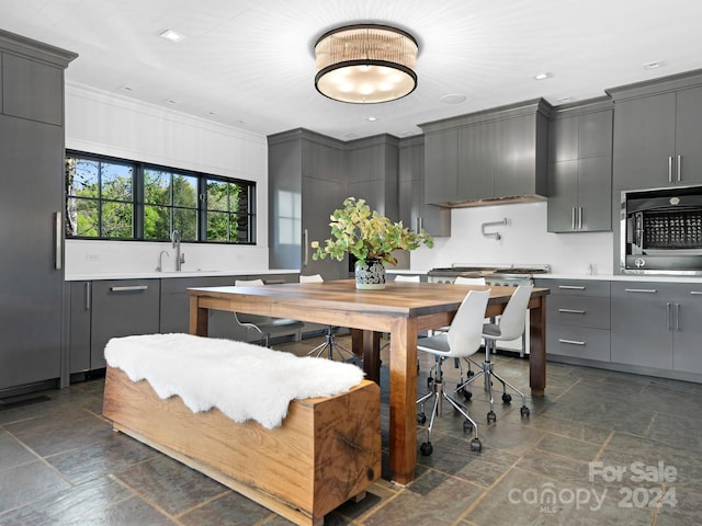 kitchen featuring appliances with stainless steel finishes, crown molding, wall chimney range hood, sink, and gray cabinets