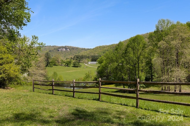 view of yard featuring a rural view, fence, and a wooded view