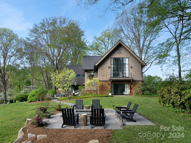 rear view of property with a patio, a yard, stone siding, and metal roof