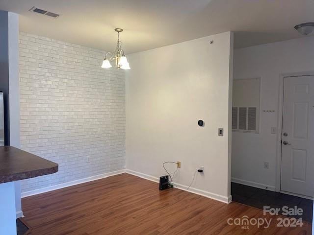 unfurnished dining area featuring dark hardwood / wood-style flooring, a chandelier, and brick wall