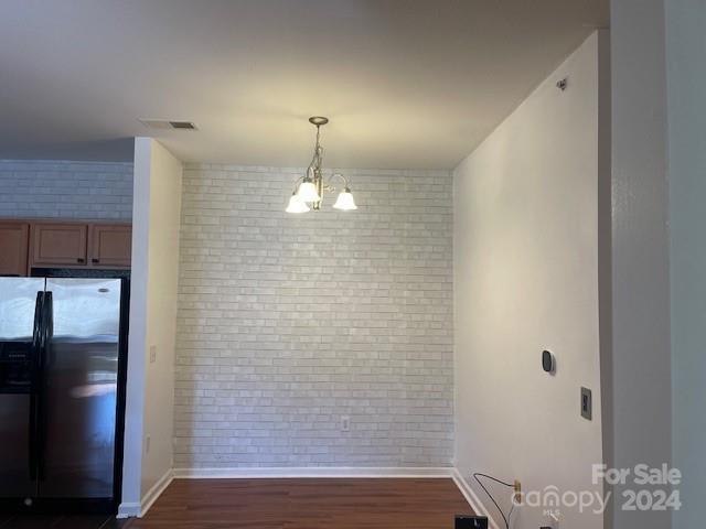 unfurnished dining area with dark wood-type flooring, brick wall, and an inviting chandelier