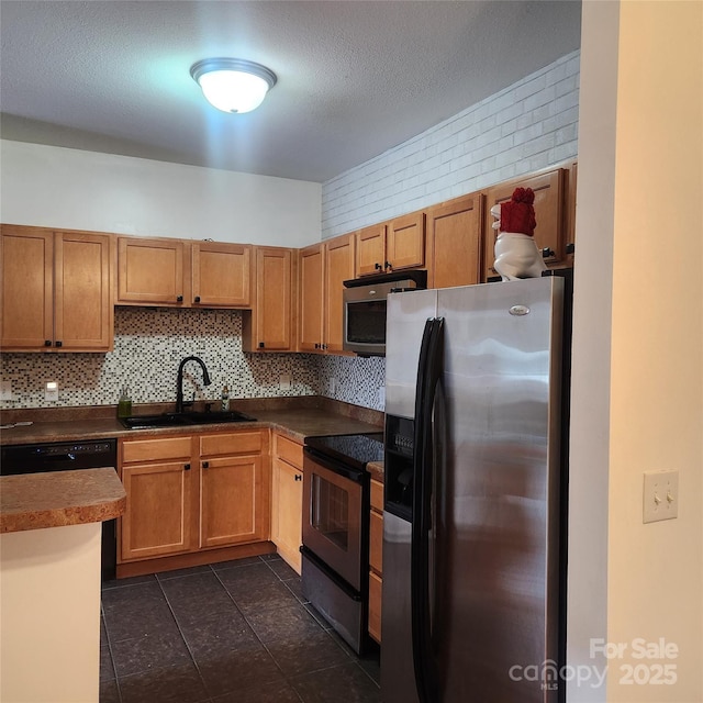 kitchen with stainless steel appliances, a sink, tasteful backsplash, dark countertops, and dark tile patterned flooring