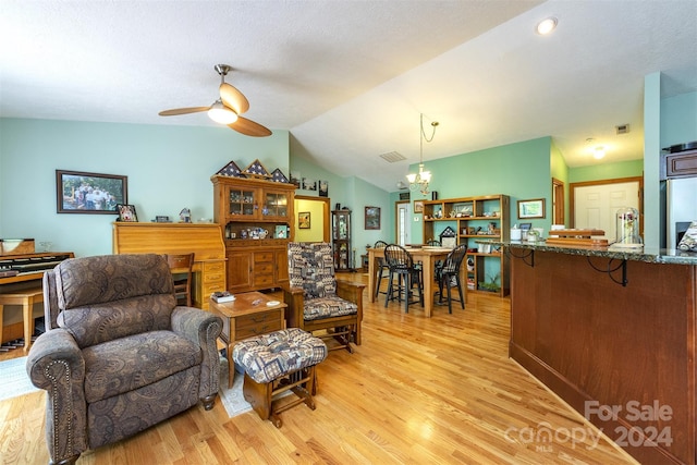 living room featuring lofted ceiling, light hardwood / wood-style floors, ceiling fan with notable chandelier, and a textured ceiling