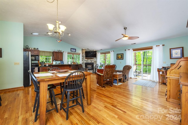 dining space featuring ceiling fan with notable chandelier, a fireplace, lofted ceiling, and light wood-type flooring