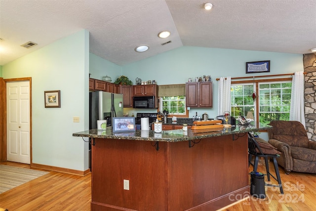 kitchen featuring stainless steel refrigerator with ice dispenser, light hardwood / wood-style flooring, vaulted ceiling, dark stone countertops, and a textured ceiling