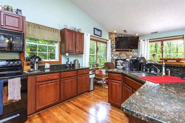 kitchen with light wood-type flooring, black appliances, sink, dark stone counters, and lofted ceiling