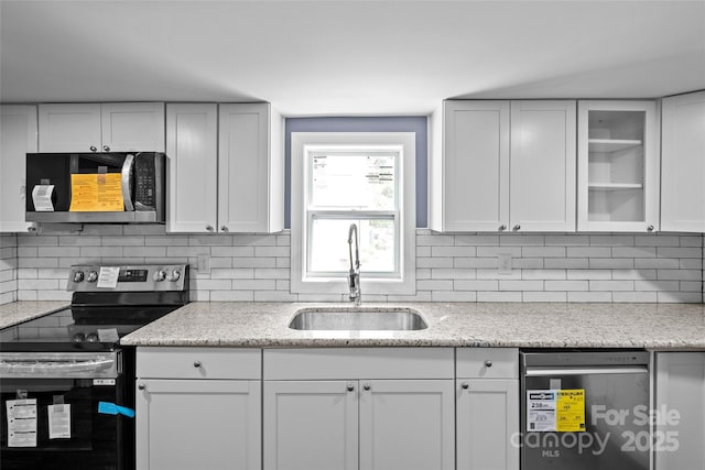 kitchen with light stone countertops, backsplash, stainless steel appliances, sink, and white cabinetry