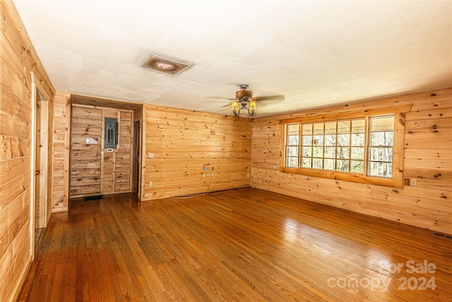 spare room with ceiling fan, dark wood-type flooring, electric panel, and wooden walls