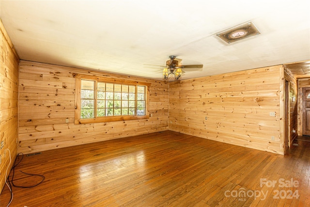 unfurnished room with ceiling fan, wood walls, and wood-type flooring