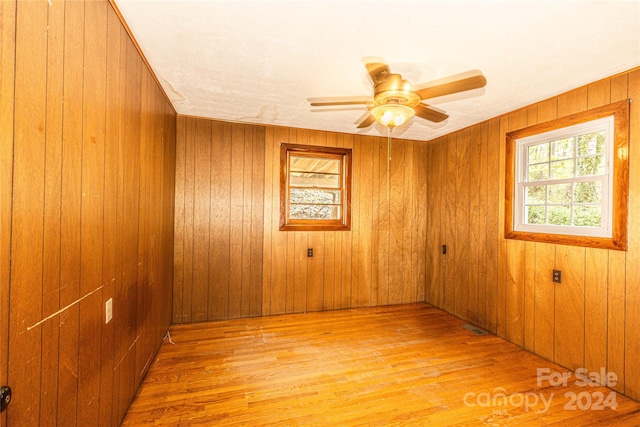 empty room featuring ceiling fan, wood walls, and light wood-type flooring