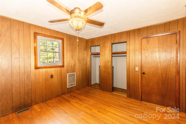 unfurnished bedroom featuring light hardwood / wood-style floors, wood walls, ceiling fan, heating unit, and multiple closets