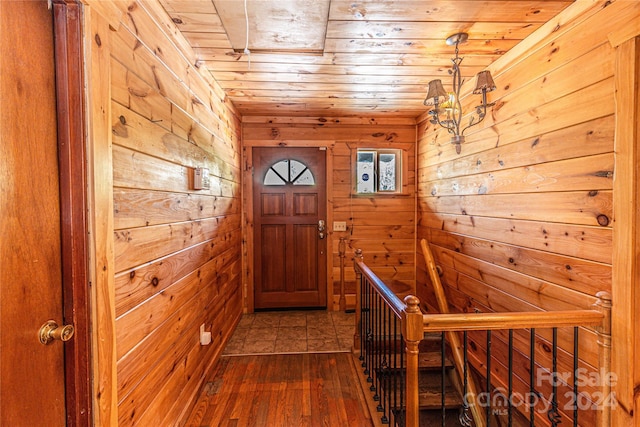 entryway featuring dark wood-type flooring, a notable chandelier, wood walls, and wood ceiling