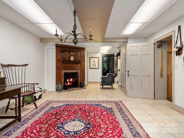 tiled living room featuring a notable chandelier, a brick fireplace, and a drop ceiling