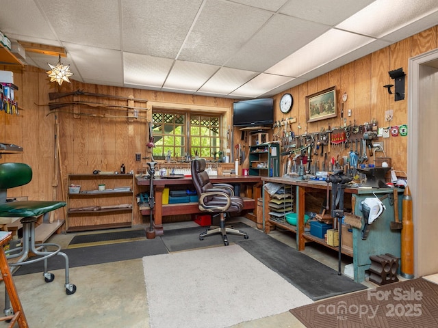 misc room with a paneled ceiling, a workshop area, wooden walls, and concrete flooring