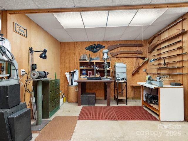 interior space with a paneled ceiling, a workshop area, and wood walls