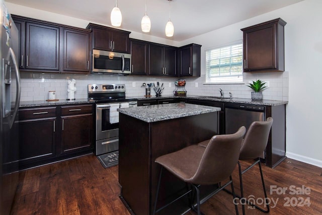 kitchen with a kitchen island, appliances with stainless steel finishes, decorative light fixtures, and dark hardwood / wood-style floors