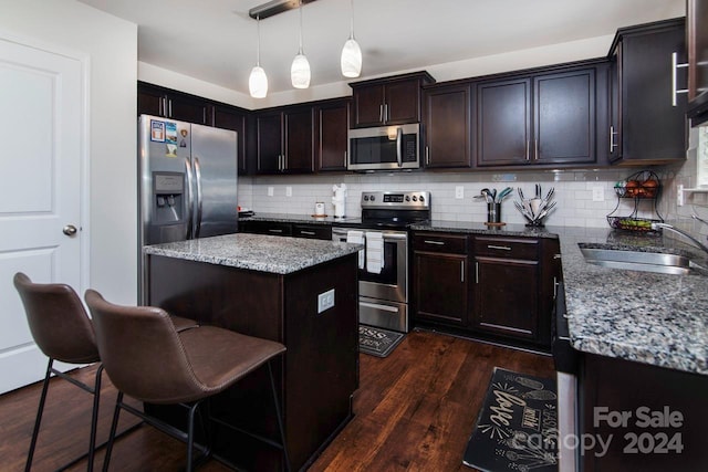 kitchen with hanging light fixtures, dark hardwood / wood-style floors, a kitchen island, light stone countertops, and appliances with stainless steel finishes